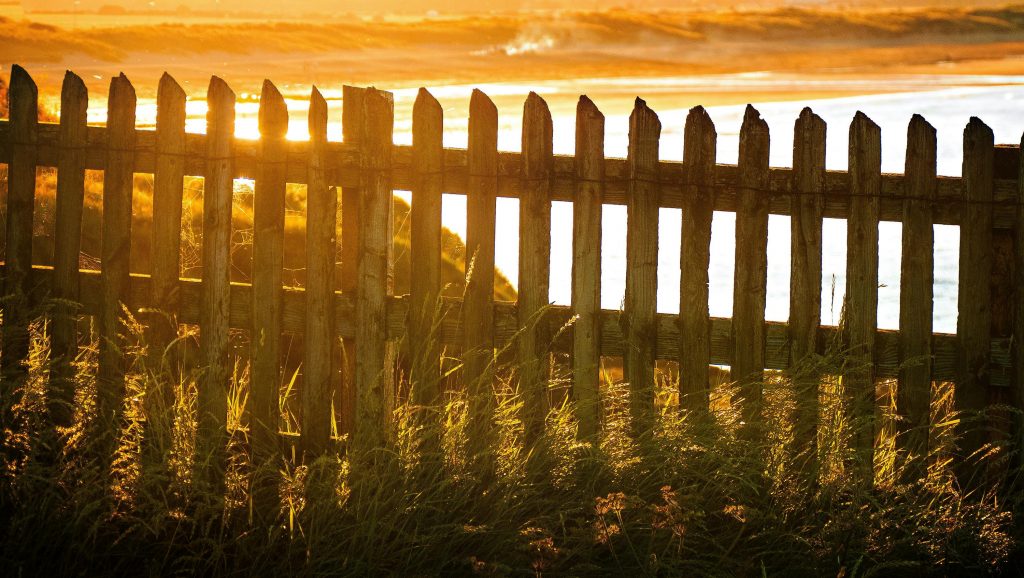 Picturesque view of sunlight streaming through a wooden fence by the beach during golden hour.